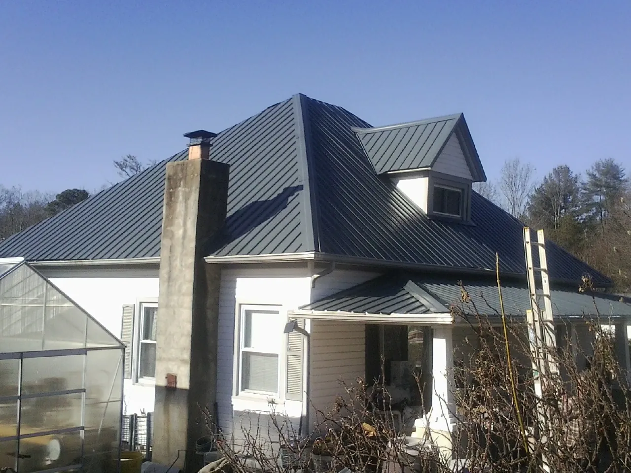 Dark blue standing seam metal roof on a white farmhouse with dormer — Slate & Tile Roof Repair by Roofing Brothers in Alamosa