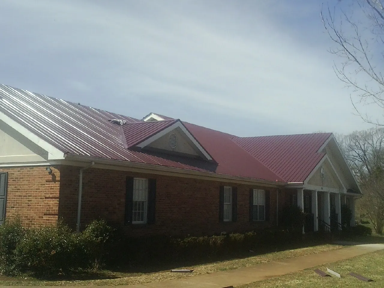 Red metal roof with gabled entries on a long brick building, from a Hail Damage Roof Repair job in Alamosa