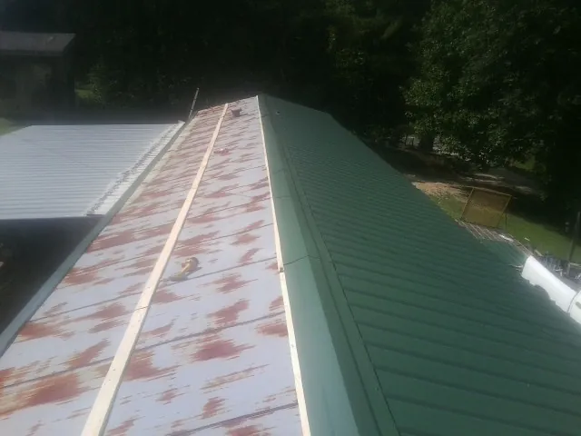 Old rusted panels beside newly installed green metal roofing — Wind Damage Roof Repair by Roofing Brothers in Alamosa