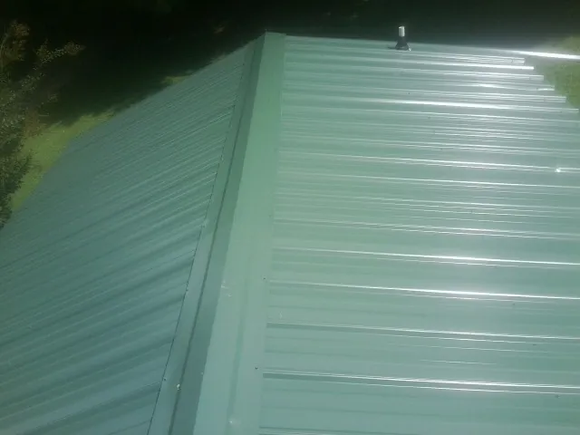New green metal panels meeting at the ridge of a roof — Flat Roof Repair work by our crew in Alamosa