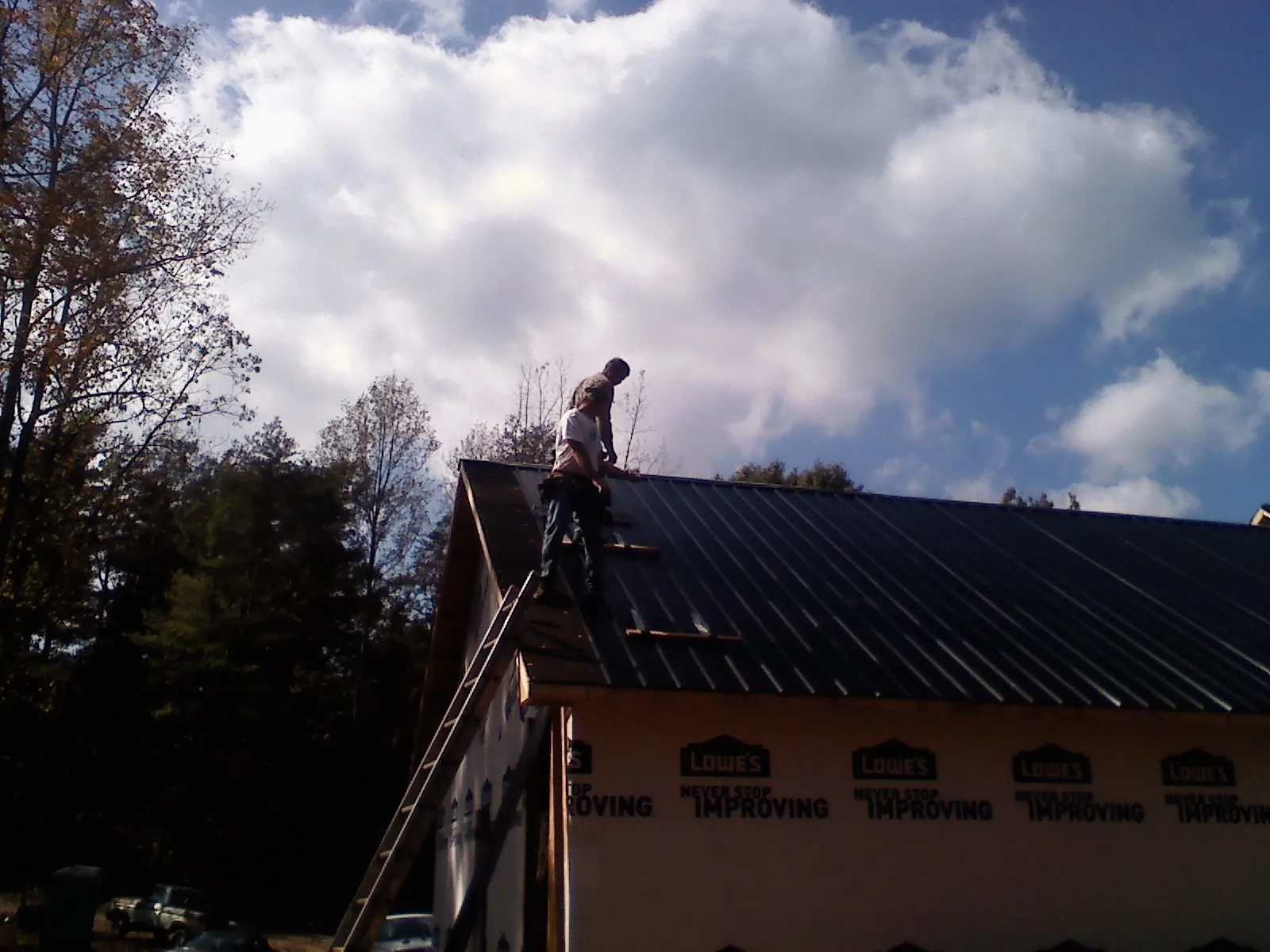 Roofer fastening dark metal panels high against a cloudy sky, from a Roof Inspection job in Alamosa