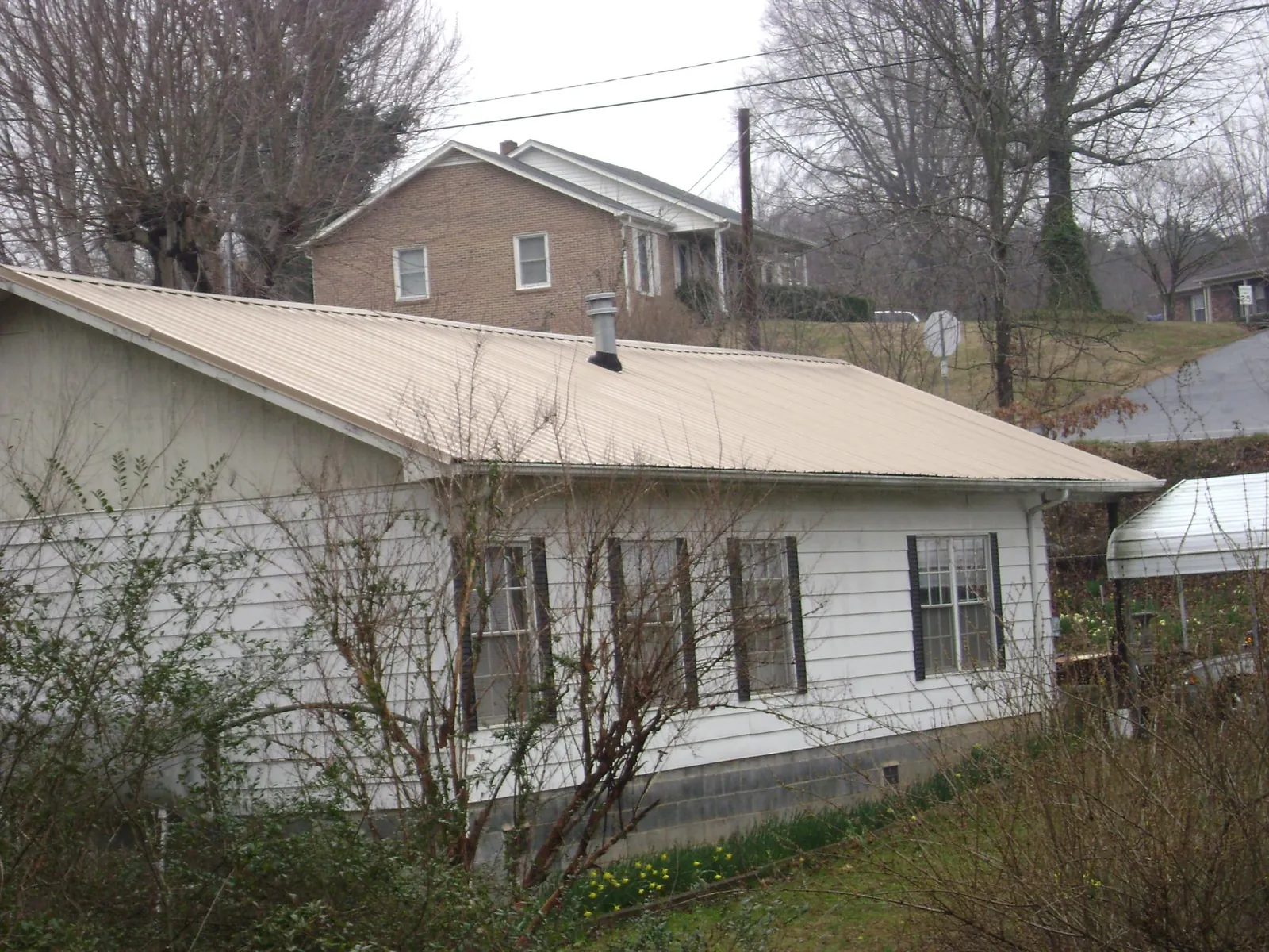 Tan metal roof on a white sided house set into a hillside — Commercial Roofing by Roofing Brothers in Alamosa