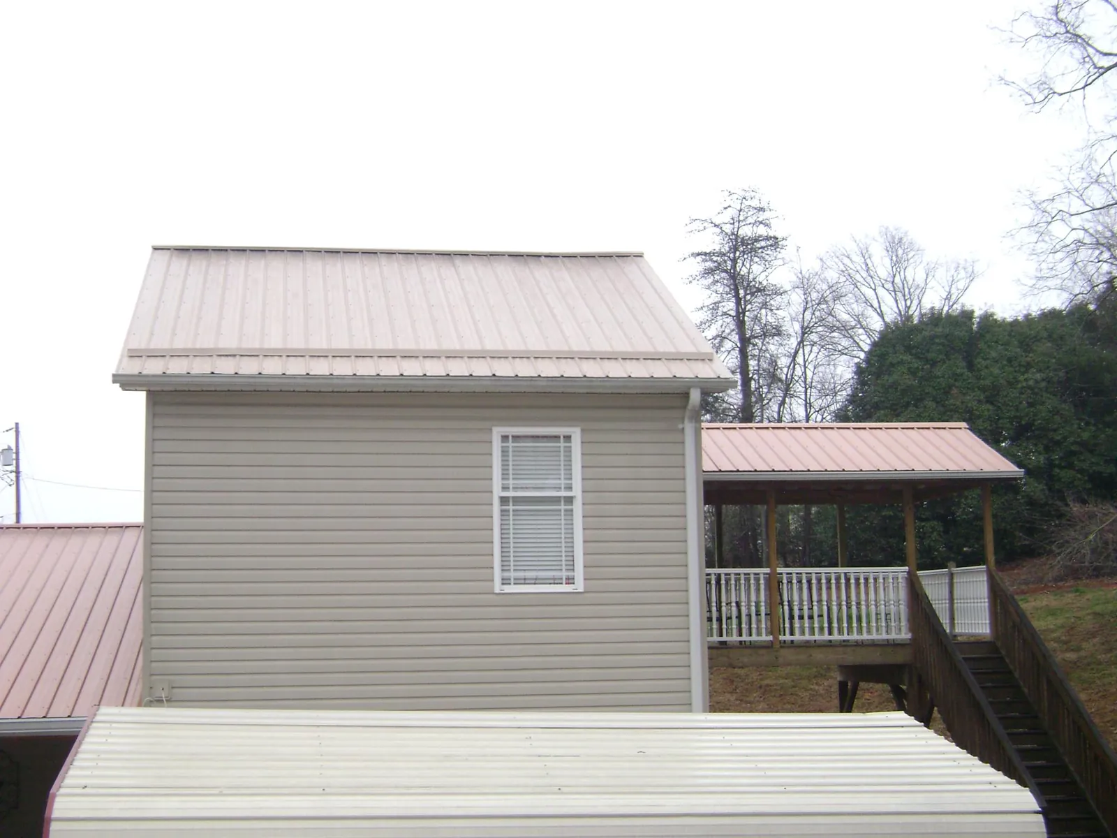 Tan metal roofs on a two story addition and attached porch, from a Roof Replacement job in Alamosa